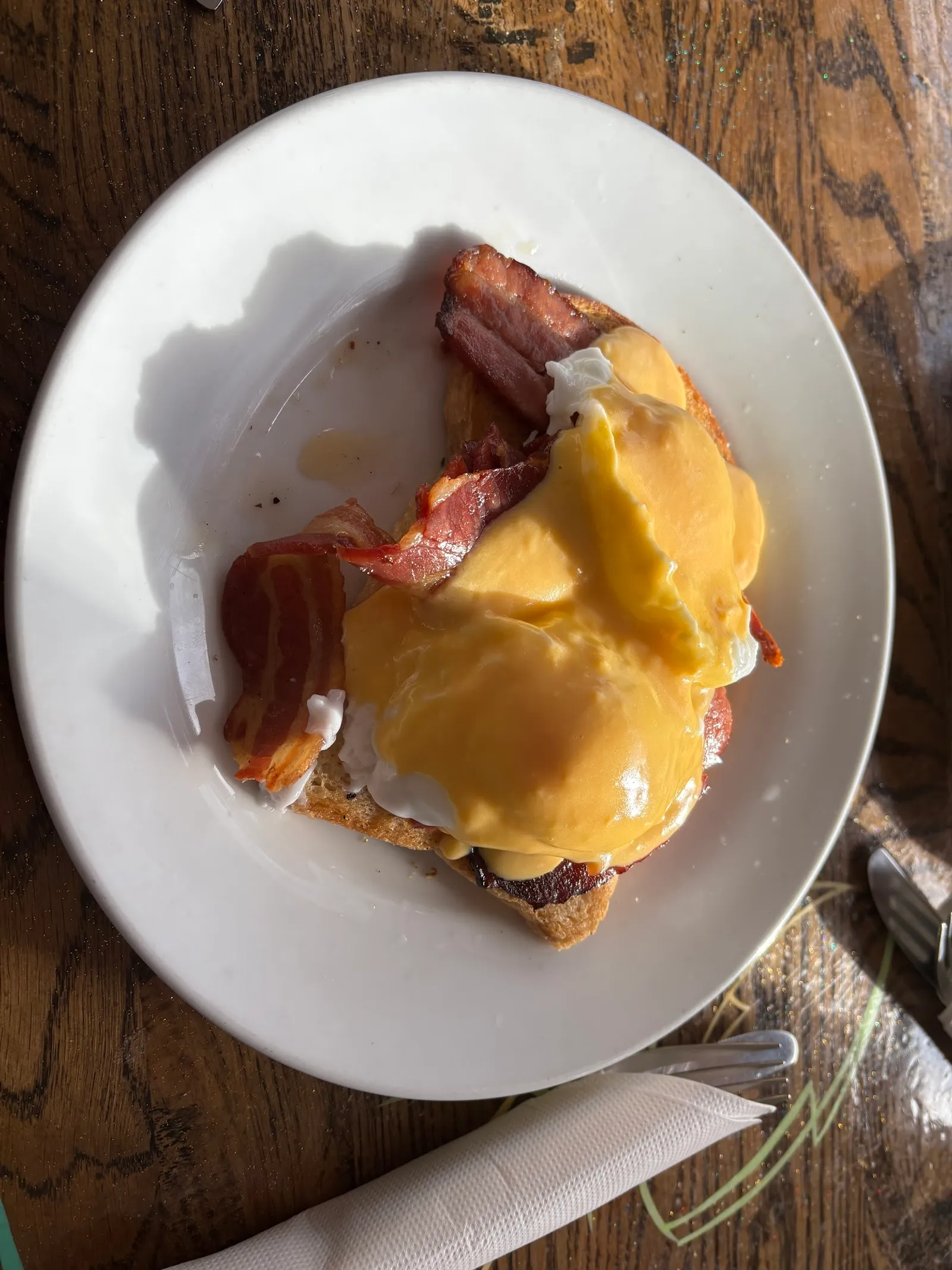 Eggs benedict with hollandaise, bacon and sourdough on white plate at Cafe Sari
